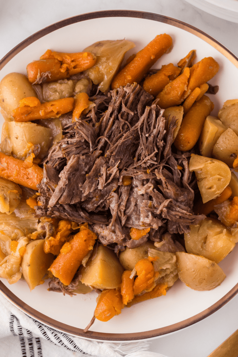 Assembled pot roast bowl with shredded beef over mashed potatoes, roasted vegetables tucked around the edge and gravy poured over