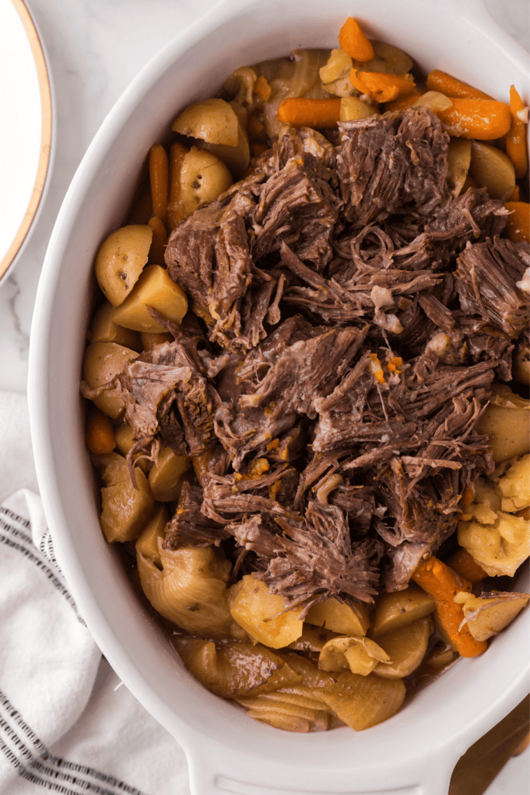 Overhead view of a Denny's style pot roast bowl with shredded beef, mashed potatoes, roasted vegetables and dinner bread