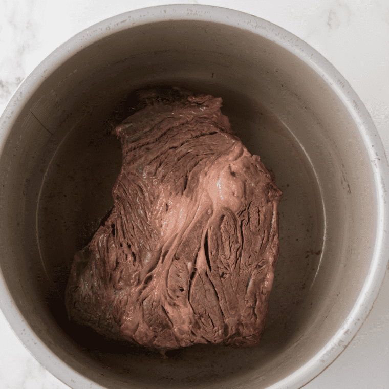 Seasoned chuck roast searing in a hot skillet with a deep brown crust forming on the underside