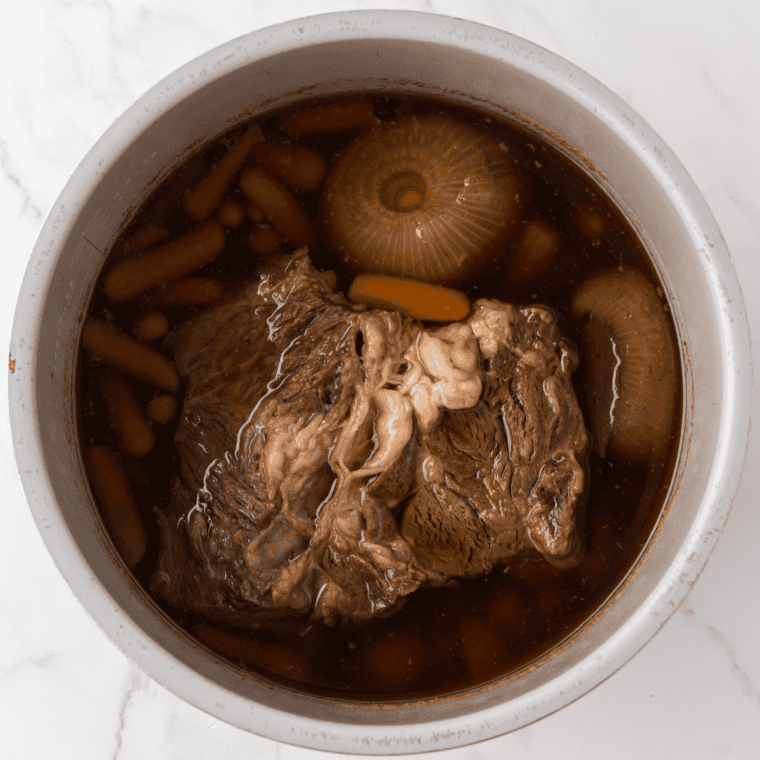 Fully cooked pot roast in a slow cooker, fork-tender and pulling apart at the edges after eight hours