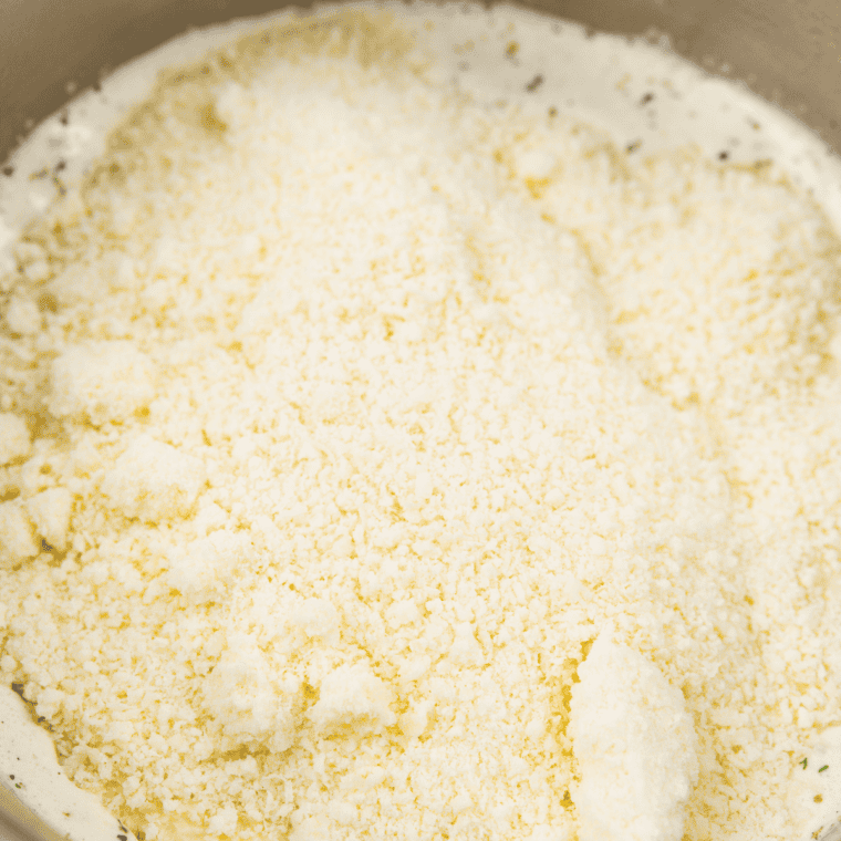 Freshly grated Parmesan being whisked into Alfredo sauce off the heat