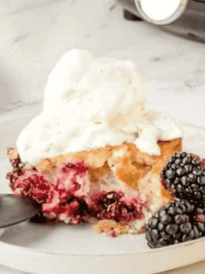 Ina Garten style blackberry cobbler in a white baking dish with golden buttermilk biscuit topping and a scoop of vanilla ice cream