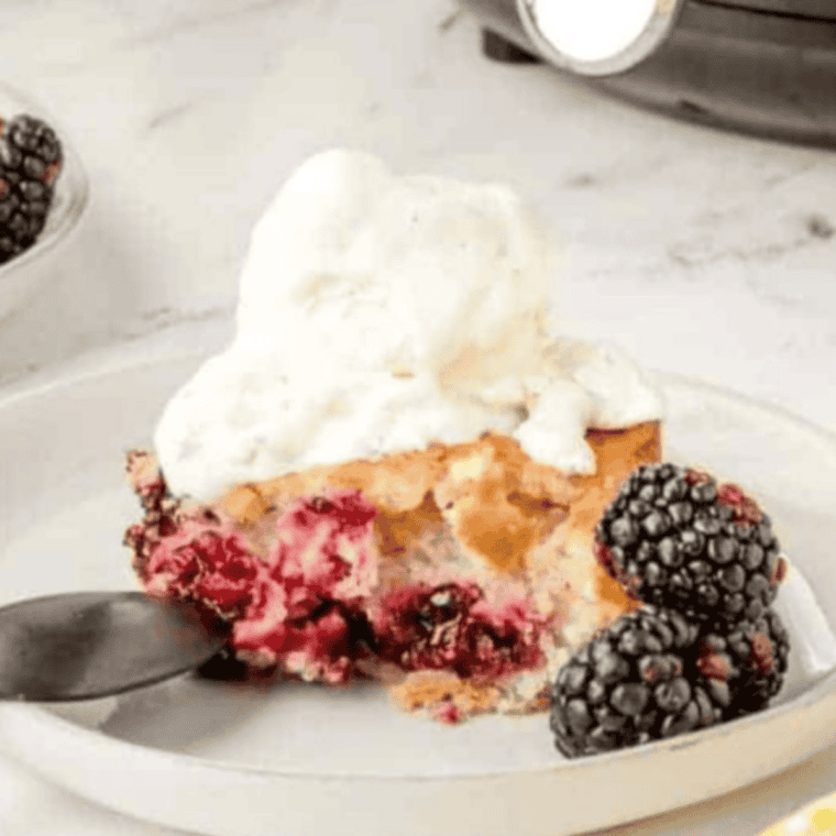 Ina Garten style blackberry cobbler in a white baking dish with golden buttermilk biscuit topping and a scoop of vanilla ice cream