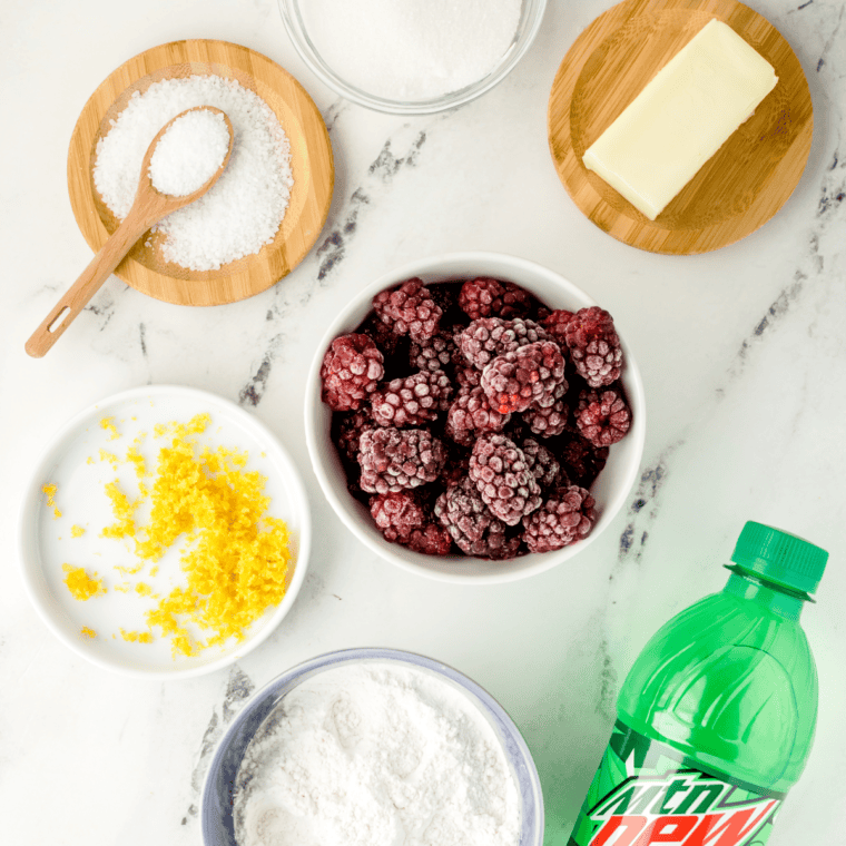 Ingredients for Ina Garten blackberry cobbler laid out on a counter: fresh blackberries, sugar, flour, cornstarch, lemon, butter, buttermilk and turbinado sugar