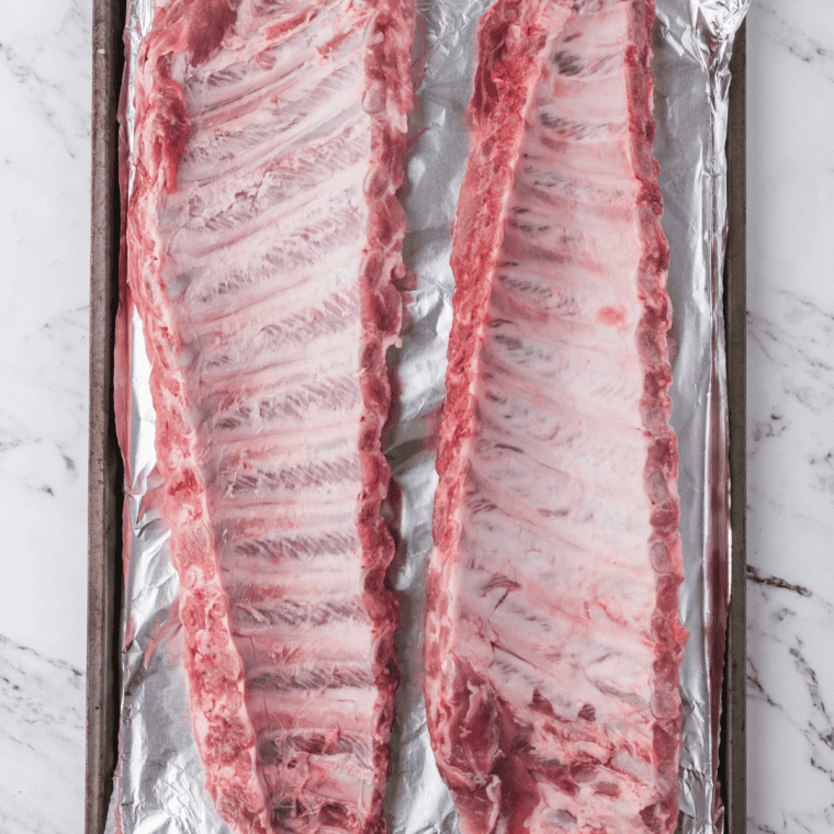 Removing the silver membrane from the back of a rack of baby back ribs with a paper towel