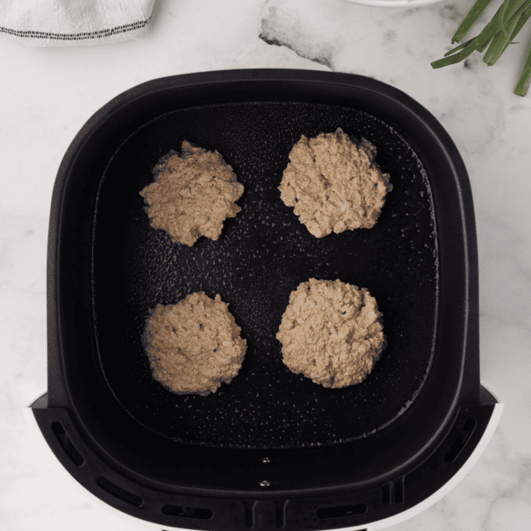 Uncooked potato pancake patties in an air fryer basket lined with parchment paper