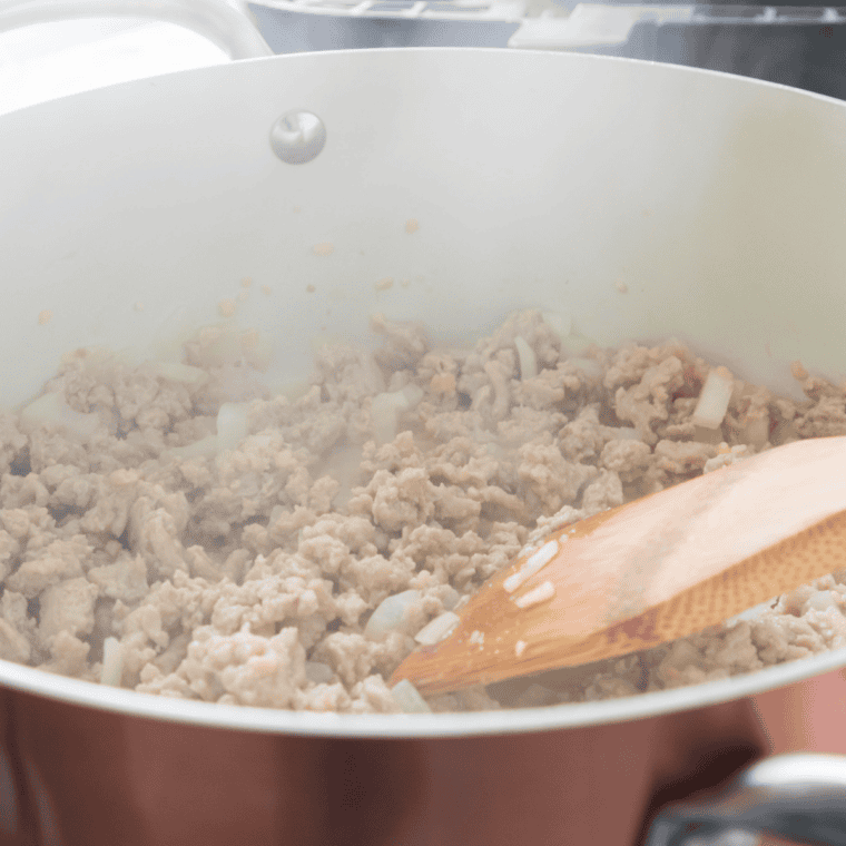 Chili powder, cumin, and oregano stirred into ground beef in a pot
