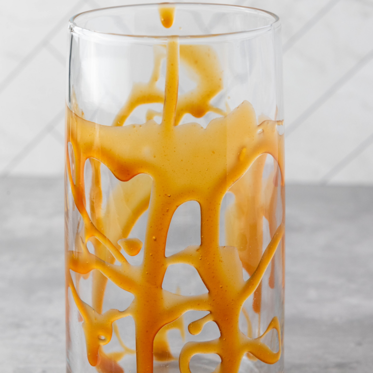 Tall glass filled to the top with ice over chocolate and caramel syrup