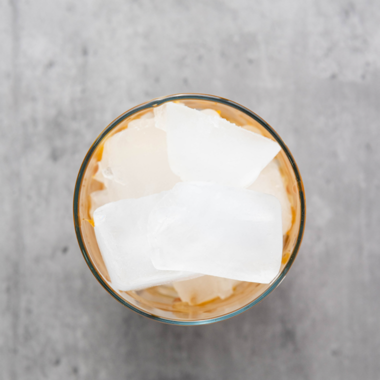 Chilled coffee being poured over ice in a glass lined with caramel drizzle