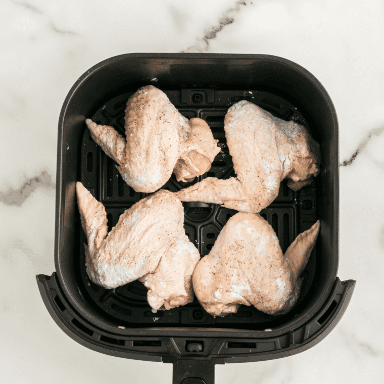 Seasoned chicken wings cooking in a single layer in an air fryer basket until golden and crispy
