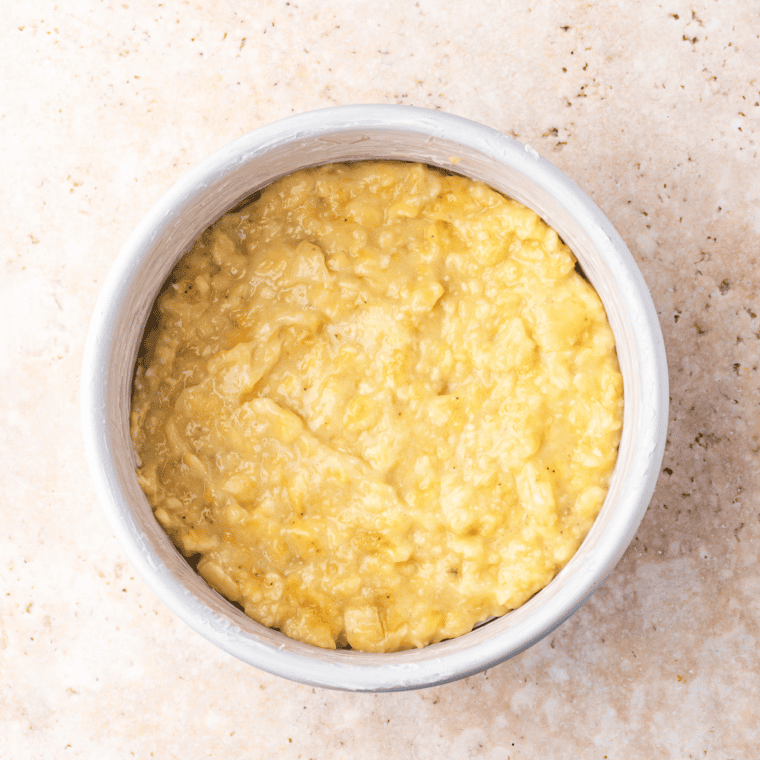 Mashed bananas spread in an even layer on the bottom of an air fryer cake pan