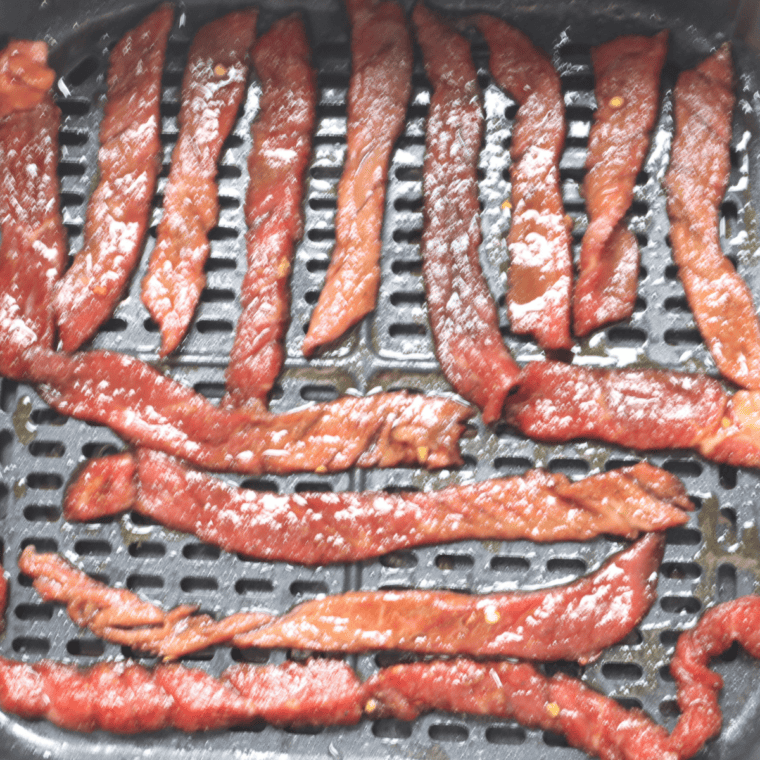 Beef jerky strips on wire racks over baking sheets for drying in the oven