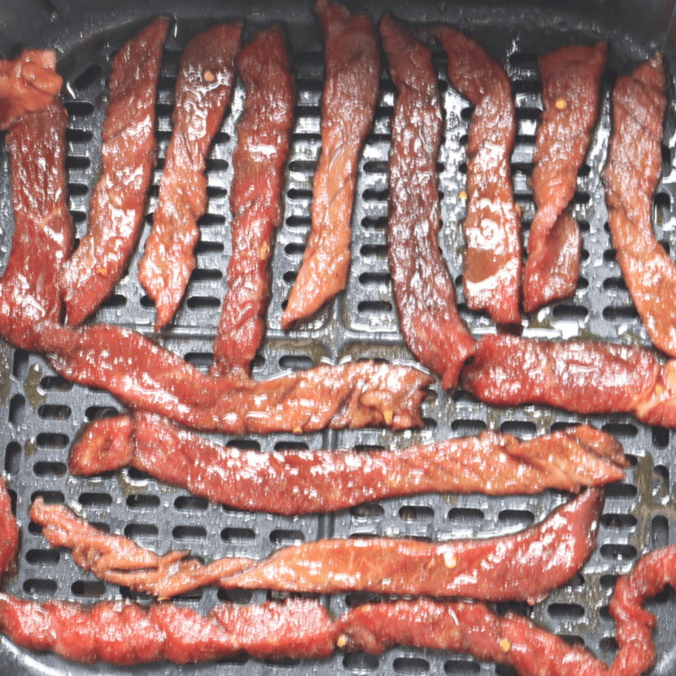 Beef jerky strips arranged in a single layer on food dehydrator trays