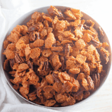Pecan praline Crispix snack mix in a white bowl, with caramel-coated cereal and toasted pecan halves