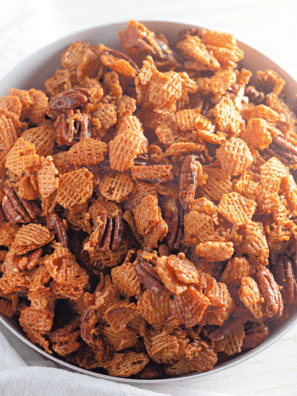 Pecan praline Crispix snack mix in a white bowl, with caramel-coated cereal and toasted pecan halves