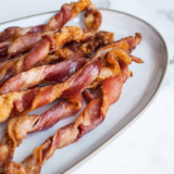 Copycat Bob Evans candied bacon with a glossy brown sugar glaze stacked on a white plate