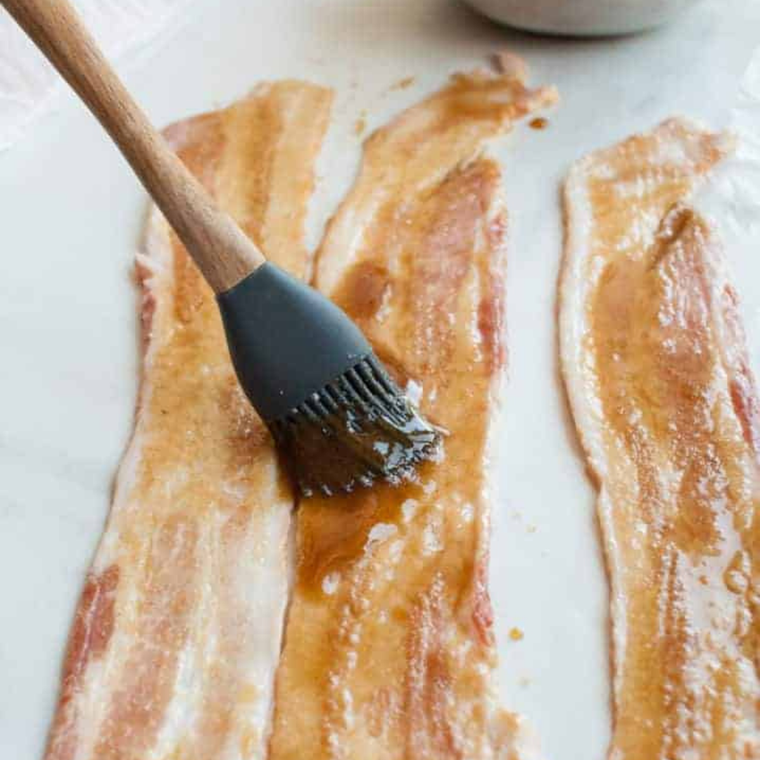 Brown sugar pressed onto raw bacon strips before baking