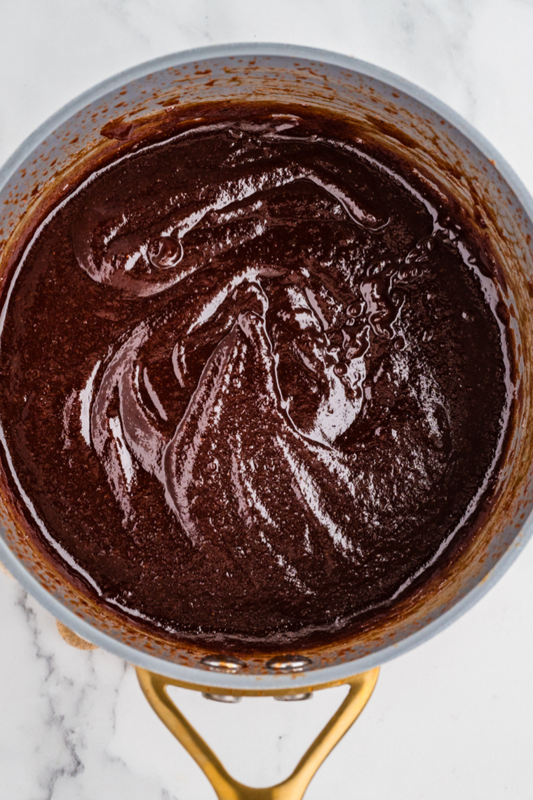 Homemade Hardee&rsquo;s BBQ sauce simmering in a saucepan and coating the back of a spoon