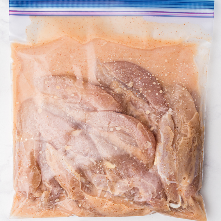 Chicken fillets soaking in buttermilk brine with hot sauce and egg in a mixing bowl