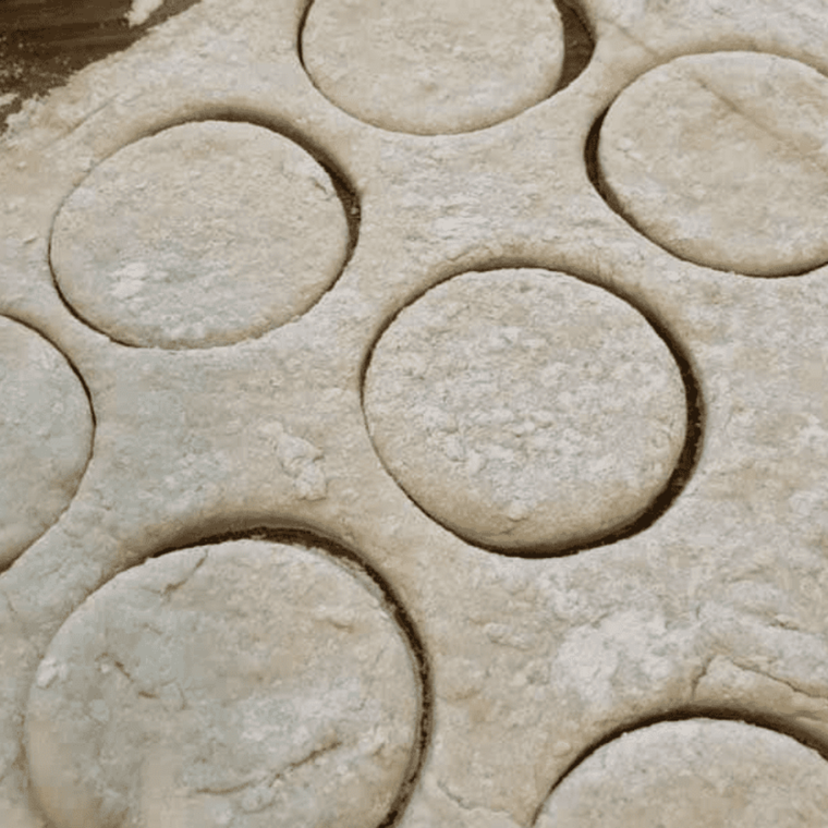 Biscuit dough patted 1 inch thick and cut with a round biscuit cutter on a floured counter