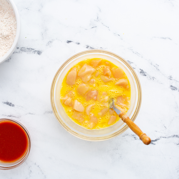Cubed chicken breast soaking in a buttermilk and egg mixture in a glass bowl.