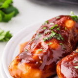Sliced slow cooker barbecue chicken breast on a white plate with a glossy BBQ glaze and caramelized edges